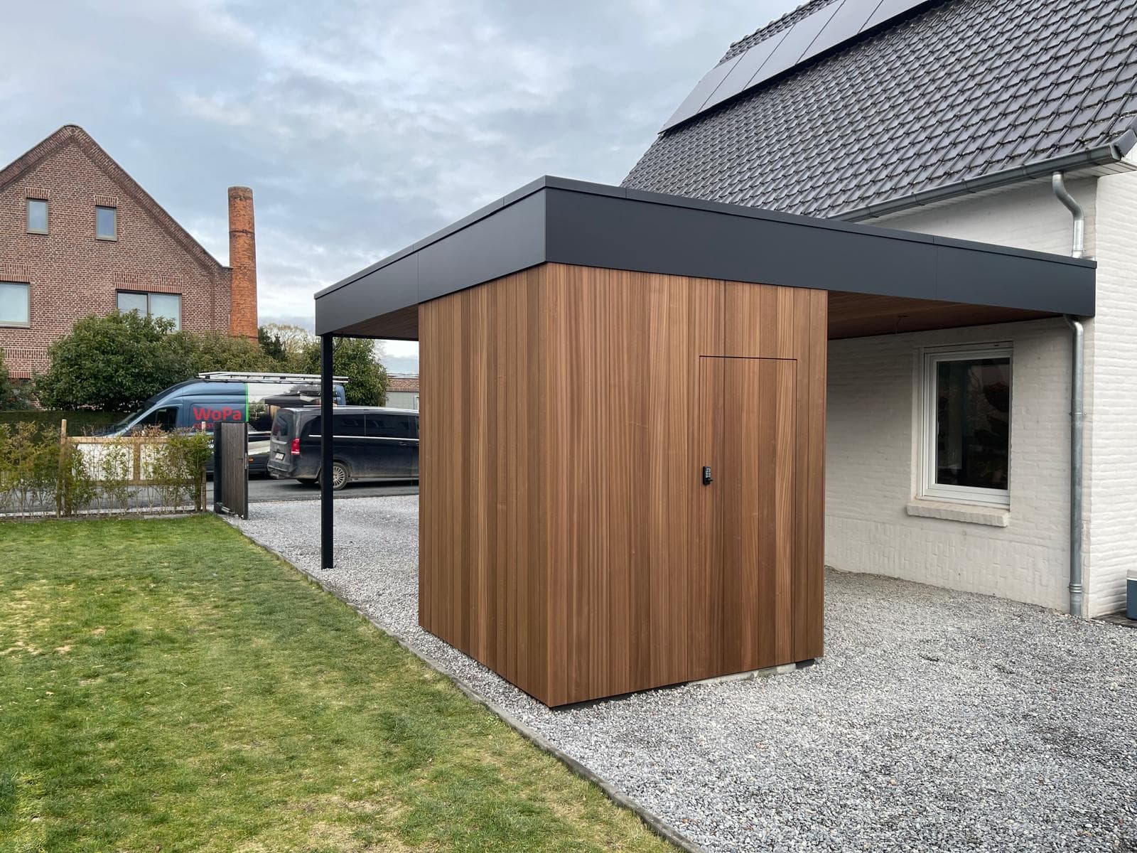 Vrijstaande houten tuinberging onder de carport met zwarte trespa dakrand