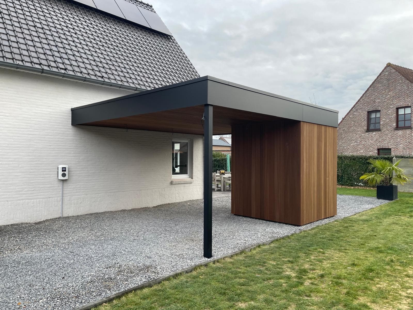 Zijaanzicht van de carport met houten bergingsblok en aangrenzend gazon