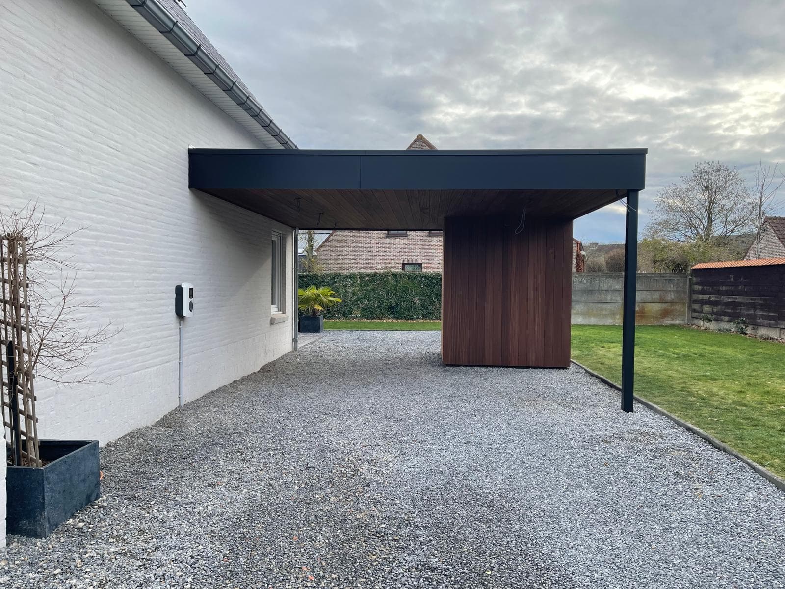 Carport gezien vanaf de oprit met grindvloer langs de witte gevel