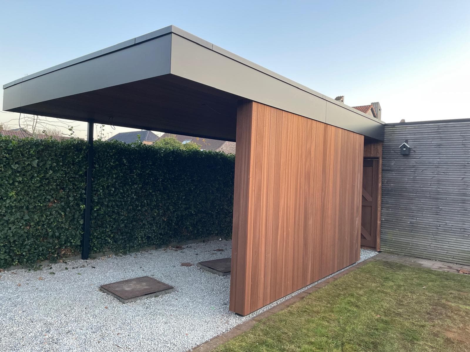 Carport van opzij met open overkapping, houten wand en zwarte trespa rand
