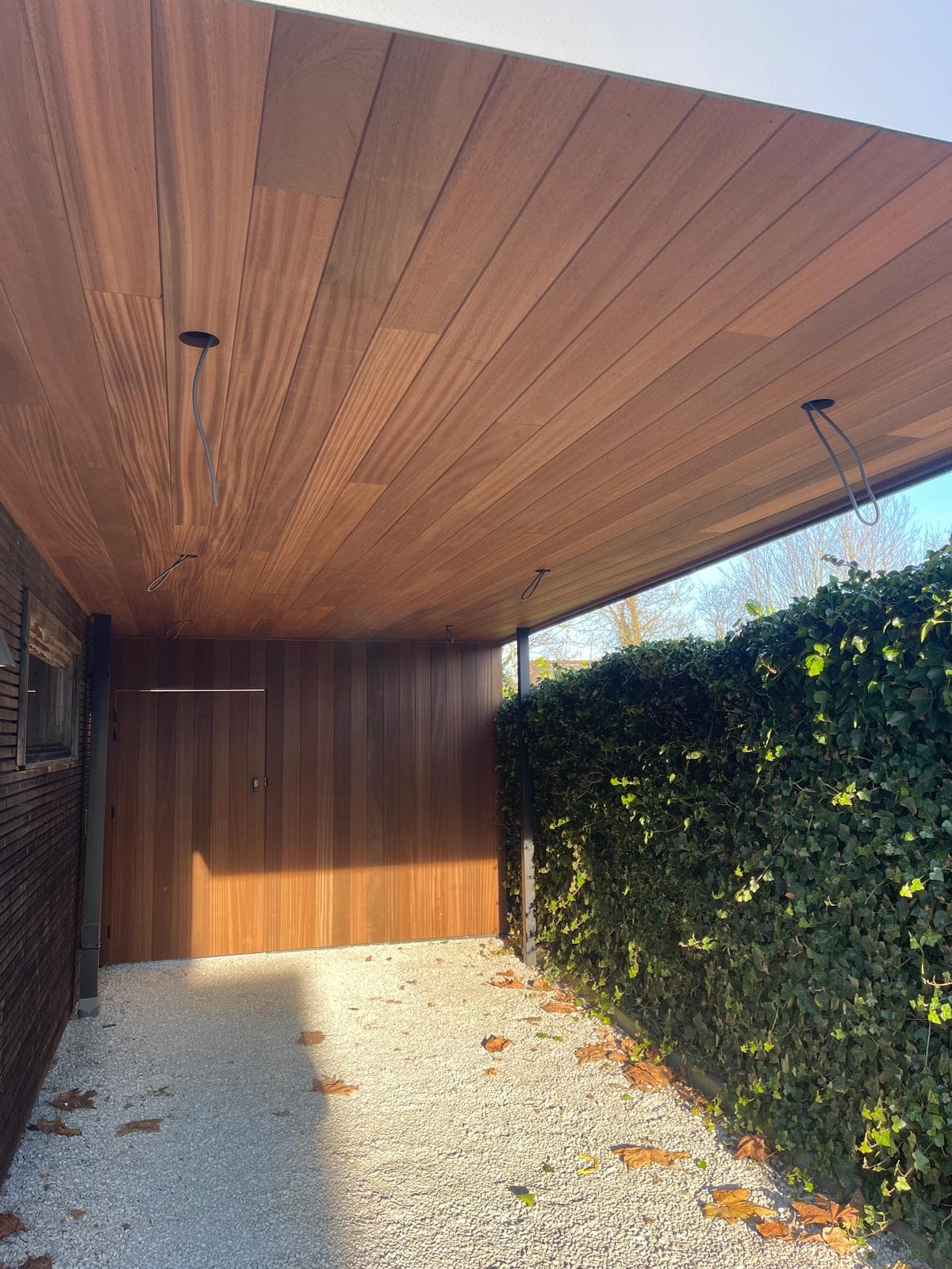Open berging met houten deur en thermohout plafond onder de carport
