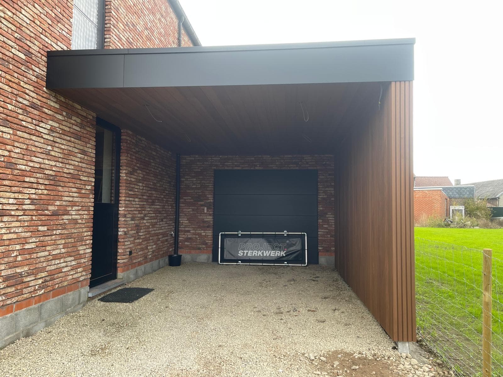 Vooraanzicht van de carport met strakke zwarte trespa rand en sectionaalpoort