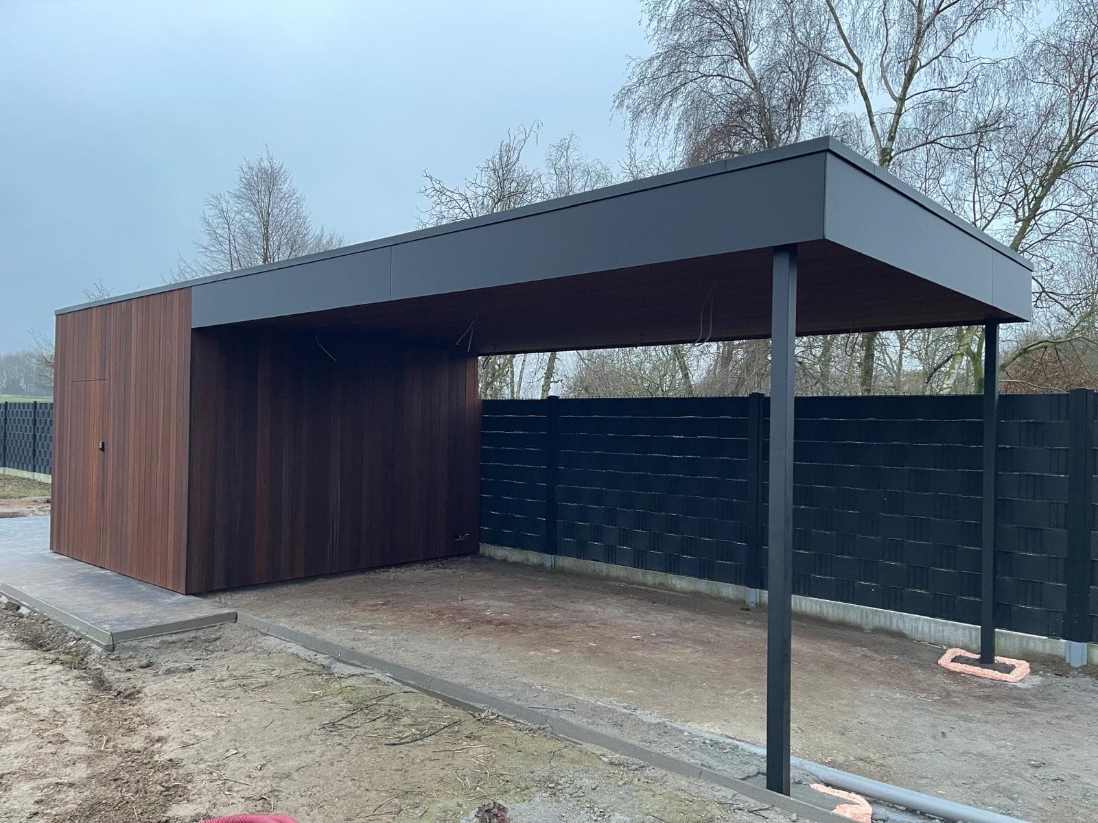 Volledig zicht op de carport met aangrenzende tuinberging in Ayous thermohout en zwarte dakrand