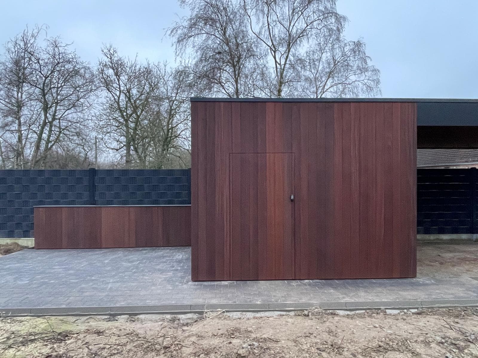 Vooraanzicht van de tuinberging met verborgen houten deur in doorlopende gevelbekleding