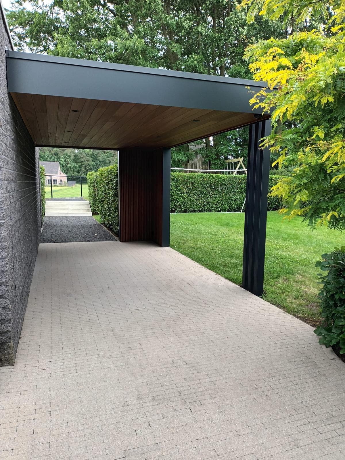 Zijaanzicht van de carport met houten plafond, zwarte trespa rand en gegroepeerde stalen sierkolommen