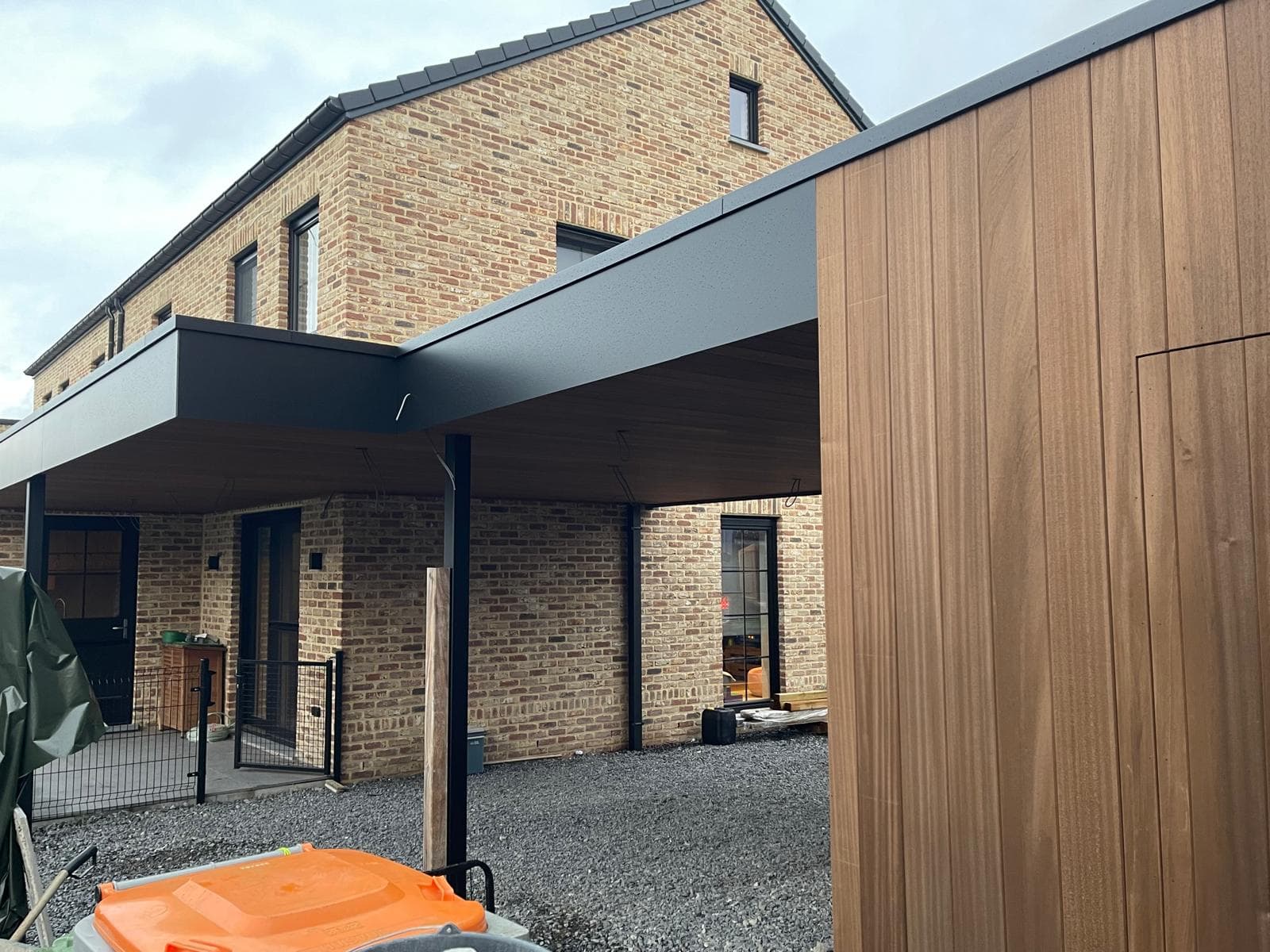 Dubbele carport met zwart plat dak die aansluit op de gevels van twee woningen