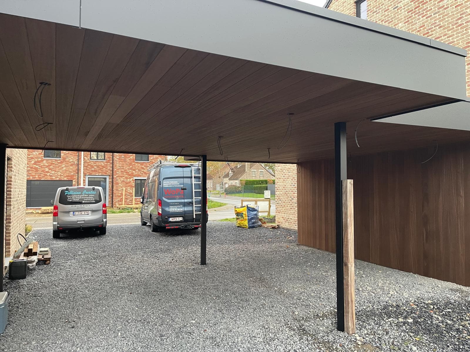 Zicht onder de carport met houten plafond, zwarte trespa en plaats voor twee wagens