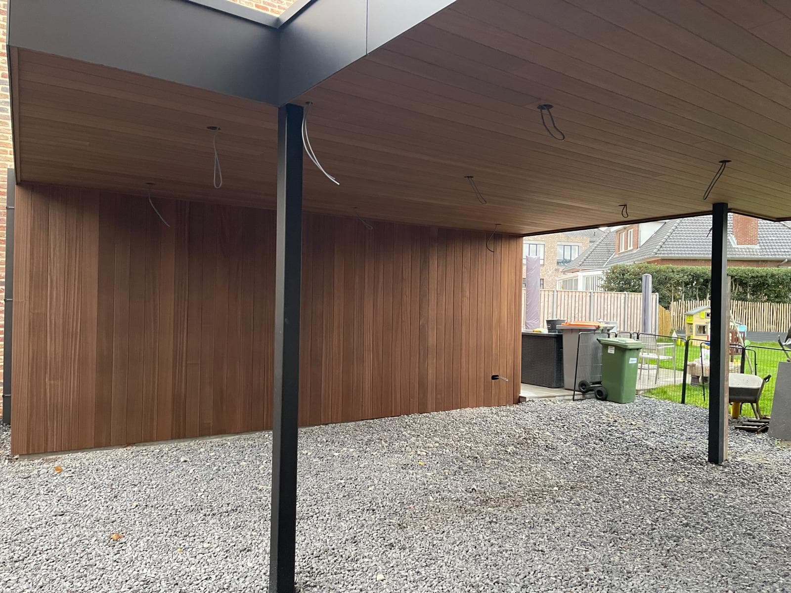 Warme houten Ayous-bekleding aan wand en plafond onder de dubbele carport
