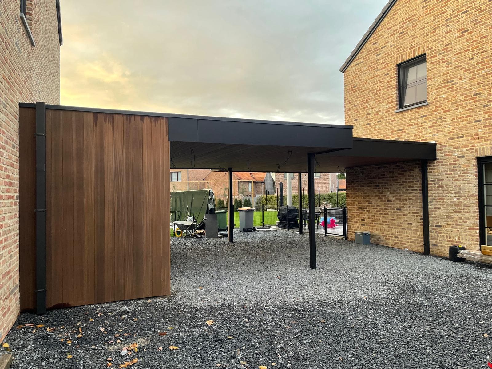 Dubbele carport met zwarte trespa en houten Ayous-bekleding tussen twee bakstenen woningen, WoPa Construction