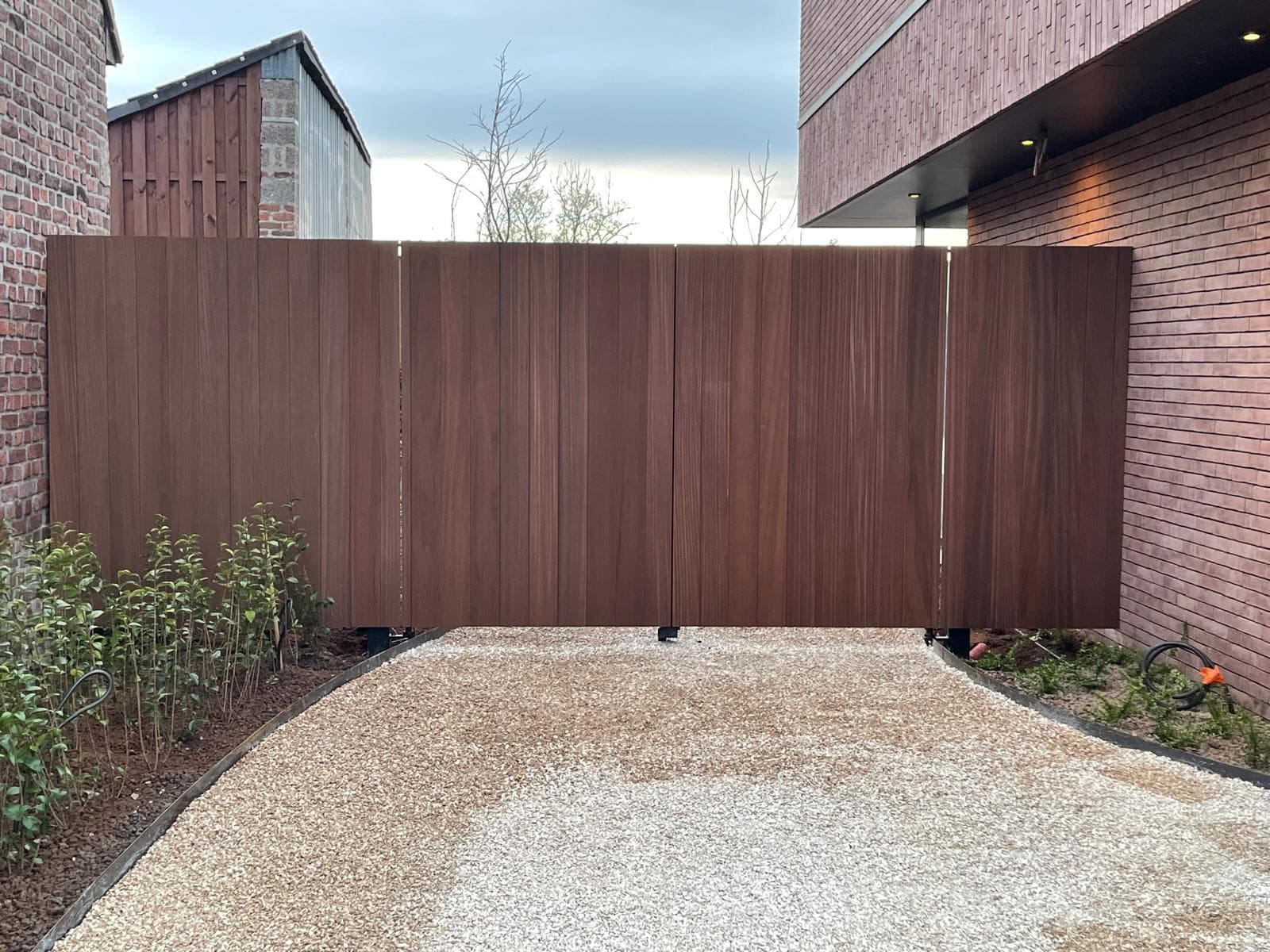 Gesloten houten poort over de oprit bij avondlicht, volledige breedte