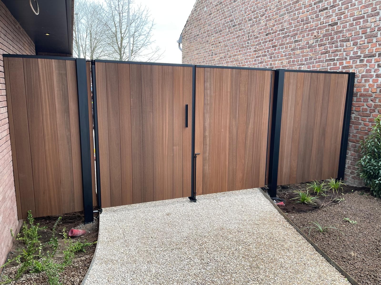 Hoekaanzicht van de houten poort met zwarte metalen palen en klink