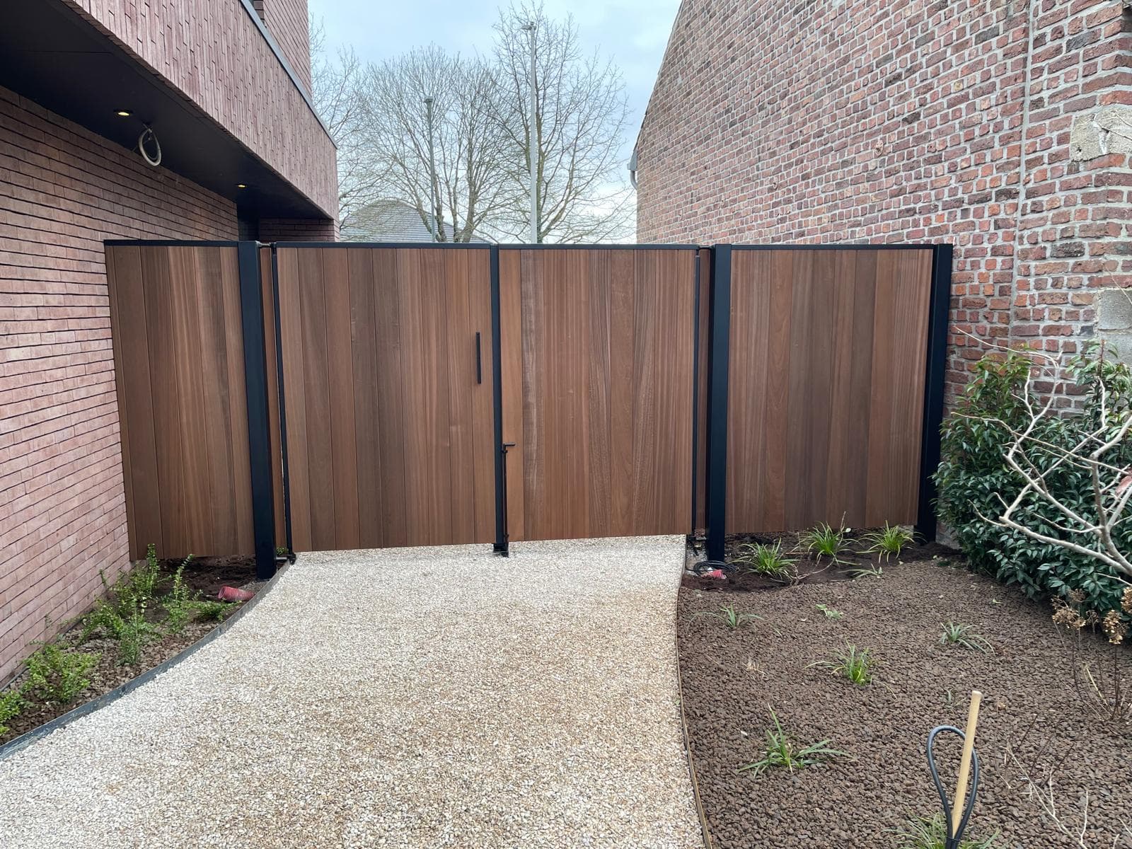 Vooraanzicht van de poort met zwart metalen frame, klink en codeklavier