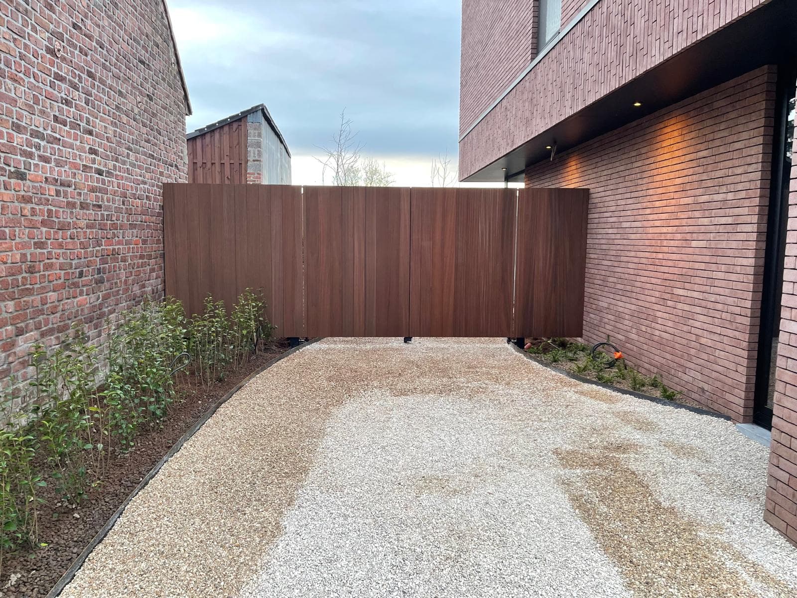 Houten poort tussen twee bakstenen woningen aan het einde van de oprit
