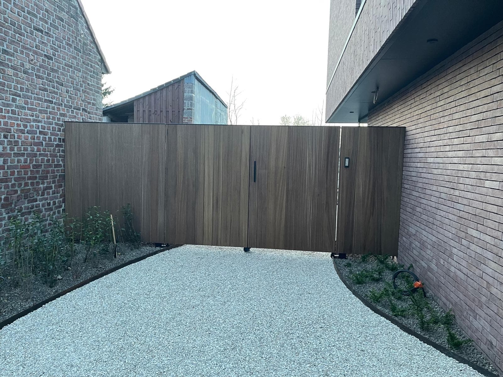 Houten inrijpoort in thermisch Ayous met zwarte metalen constructie tussen twee woningen, WoPa Construction