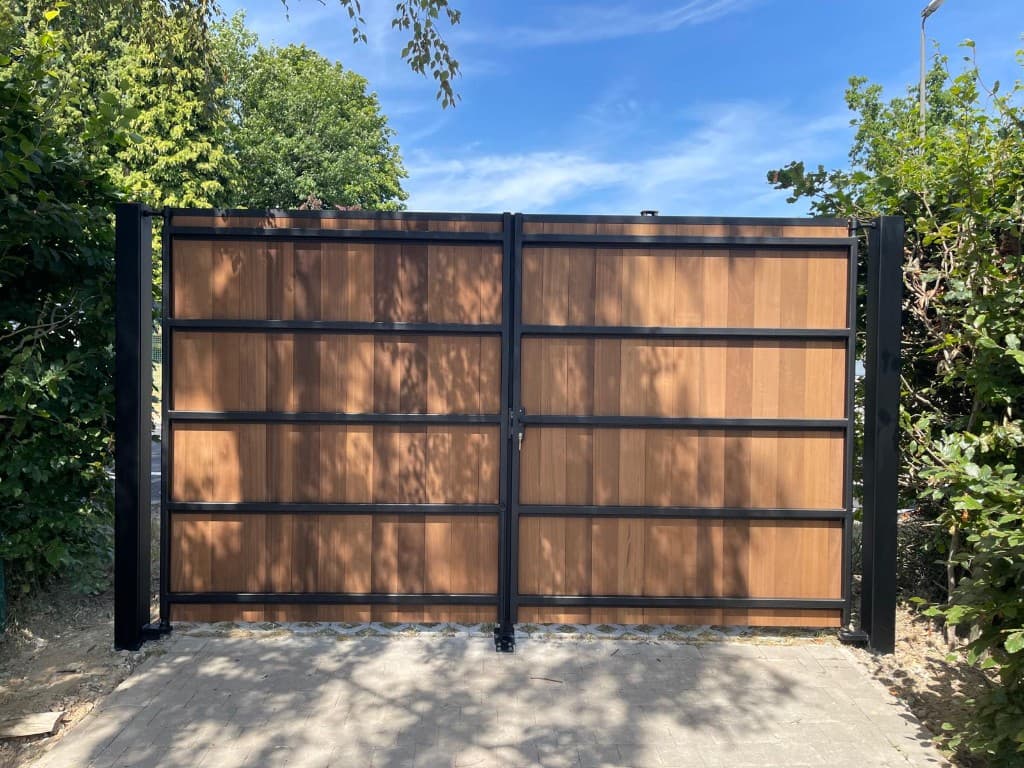 Constructiezijde van de poort met zwart staalframe en Ayous-panelen, gezien vanaf de klinkeroprit