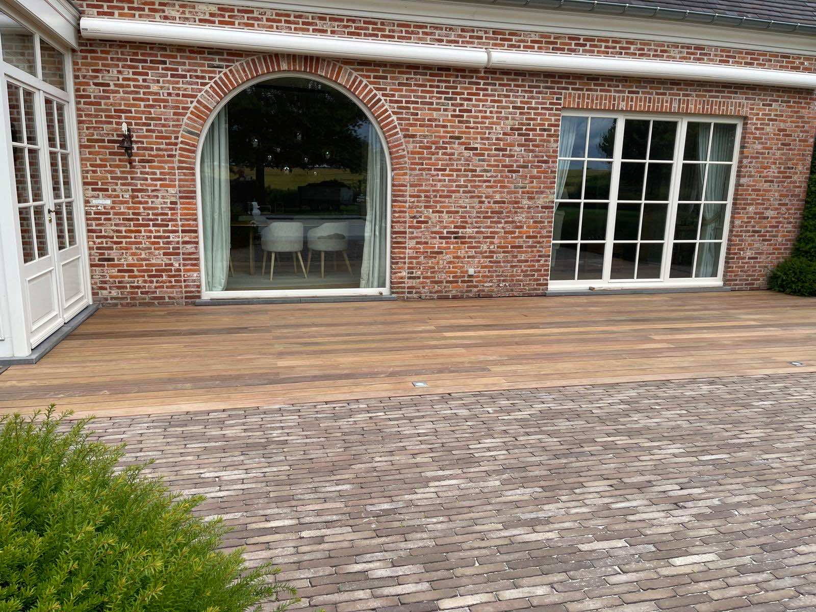 IPE-terras langs de bakstenen gevel met boograam en witte openslaande deuren