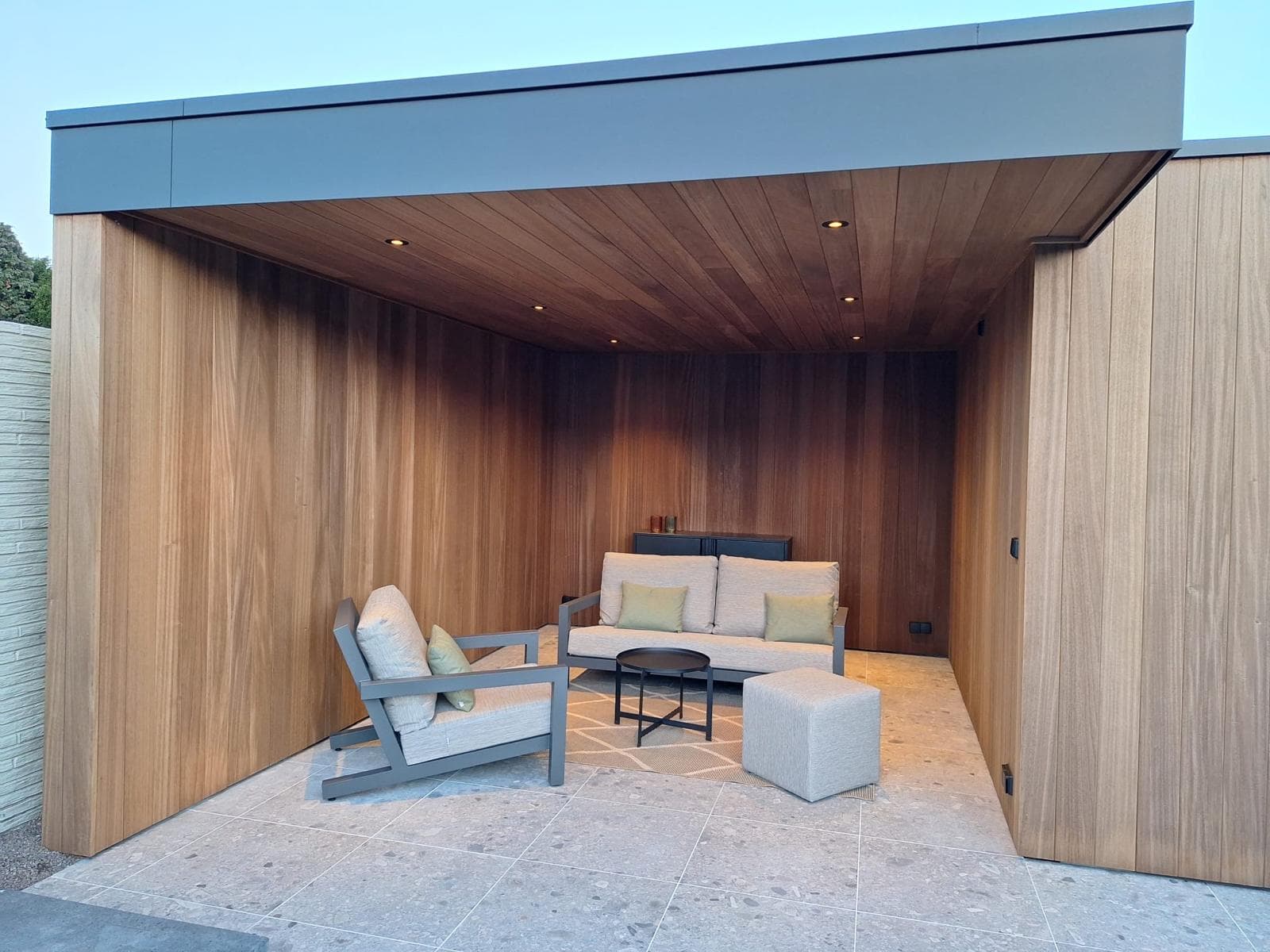 Houten overkapping met loungeset onder een warm verlicht Ayous plafond met inbouwspots