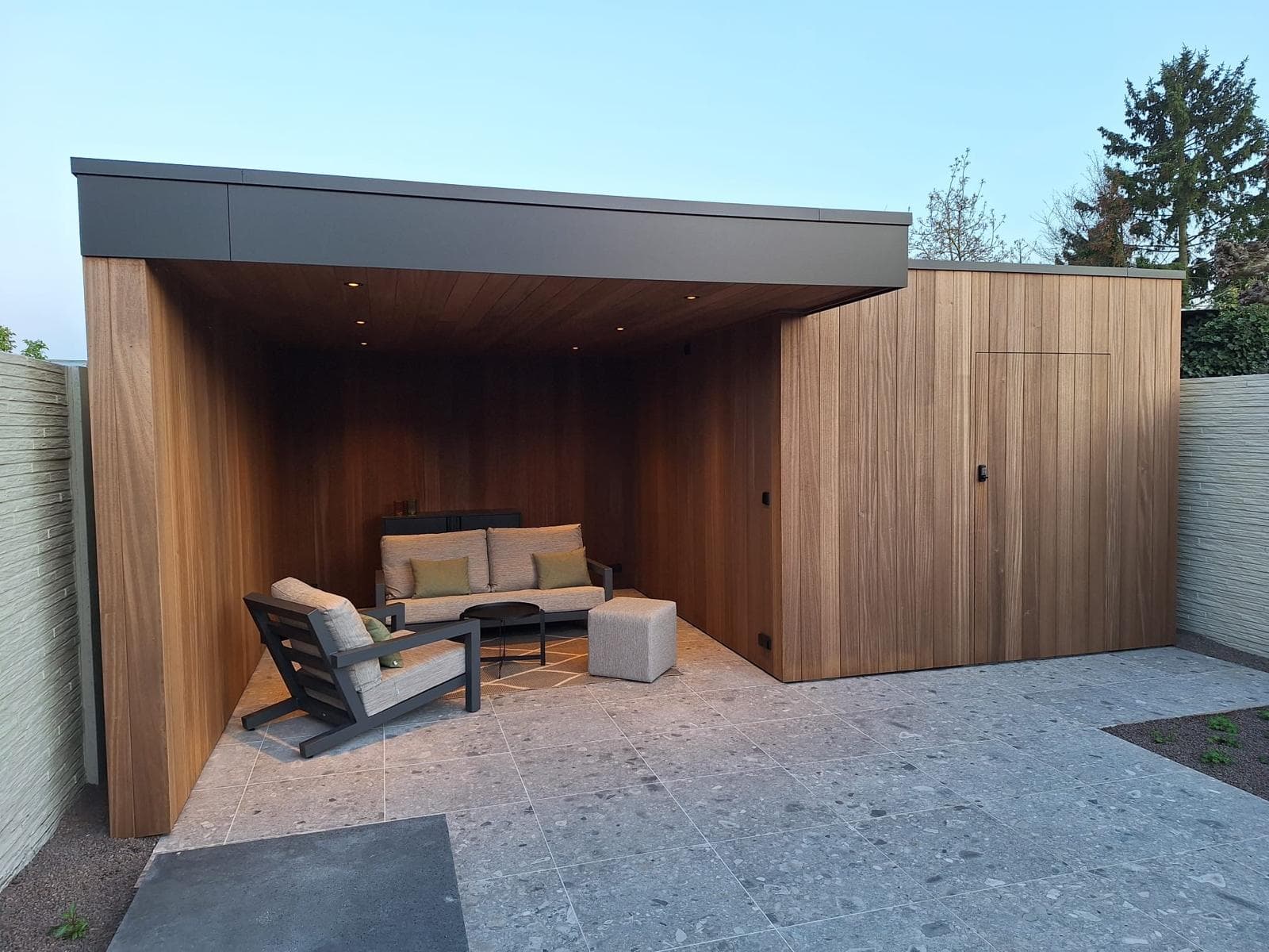 Houten overkapping in Ayous thermo met loungehoek en geïntegreerde berging in avondlicht, WoPa Construction
