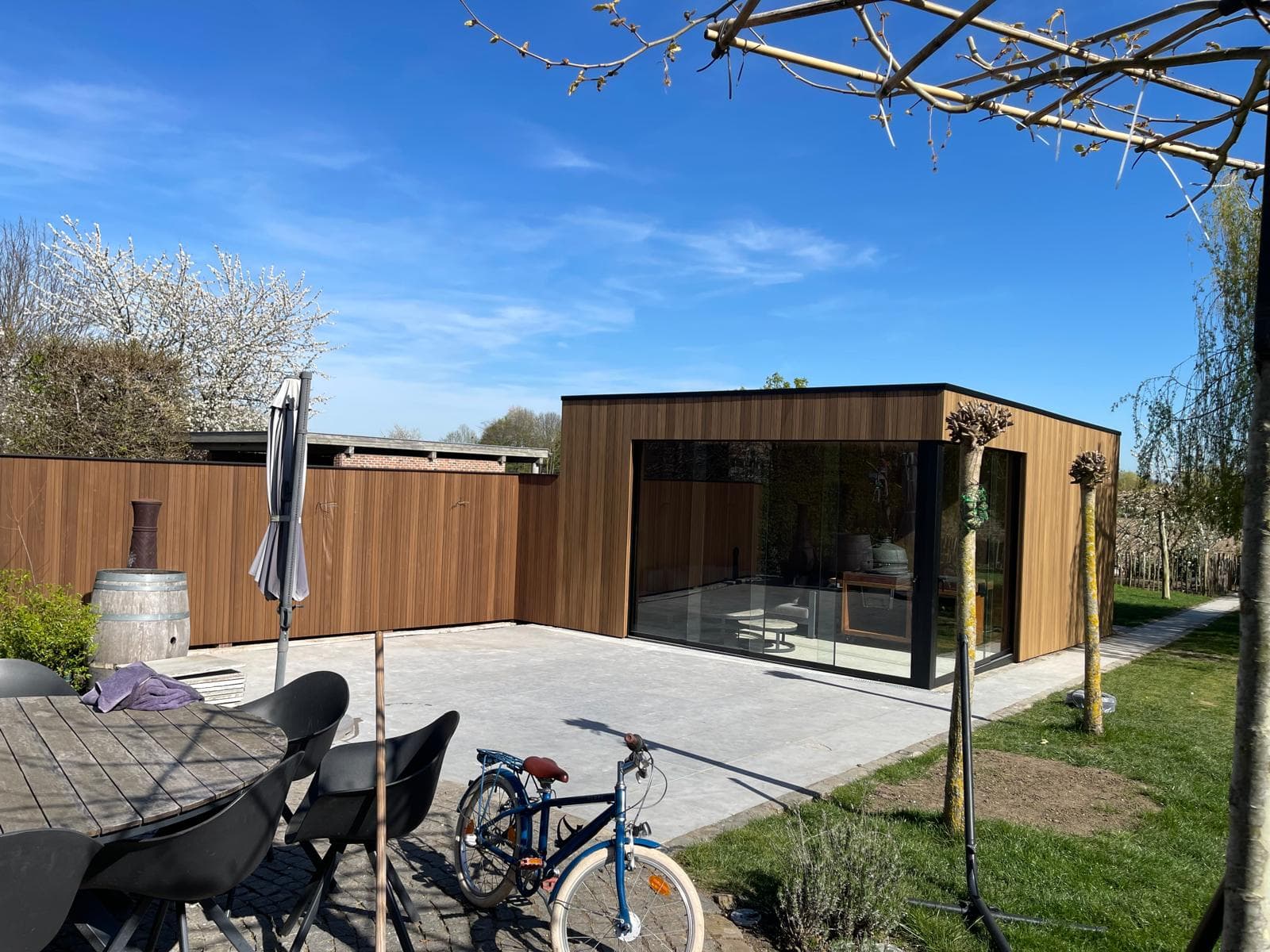 Overzicht van de tuin met terras, loungezone en de overkapping met glazen schuifwanden