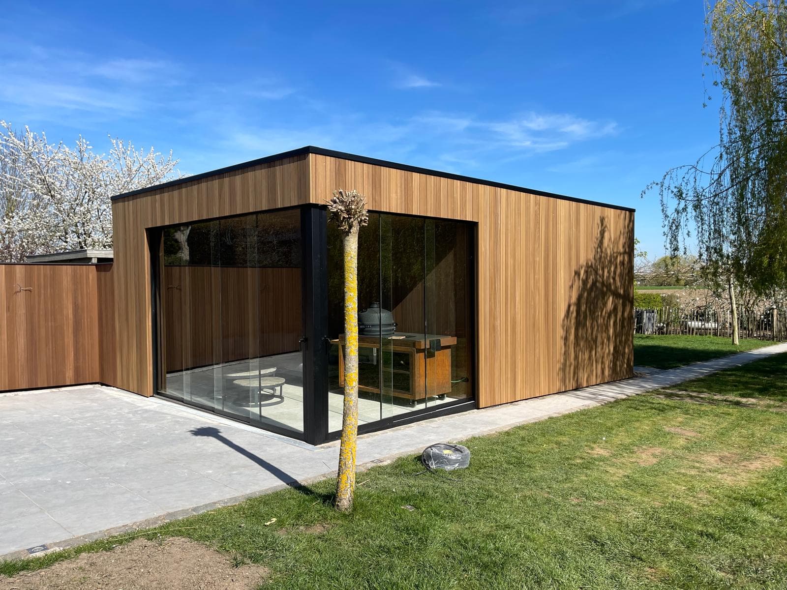 Tuinberging met overkapping in Ayous thermo en glazen schuifwanden onder een blauwe lucht, WoPa Construction