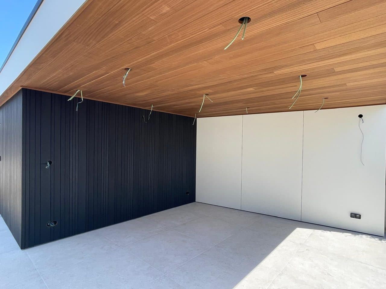 Materiaaldetail onder de overkapping: warm Ayous plafond, zwarte verticale Ayous wand en witte trespa