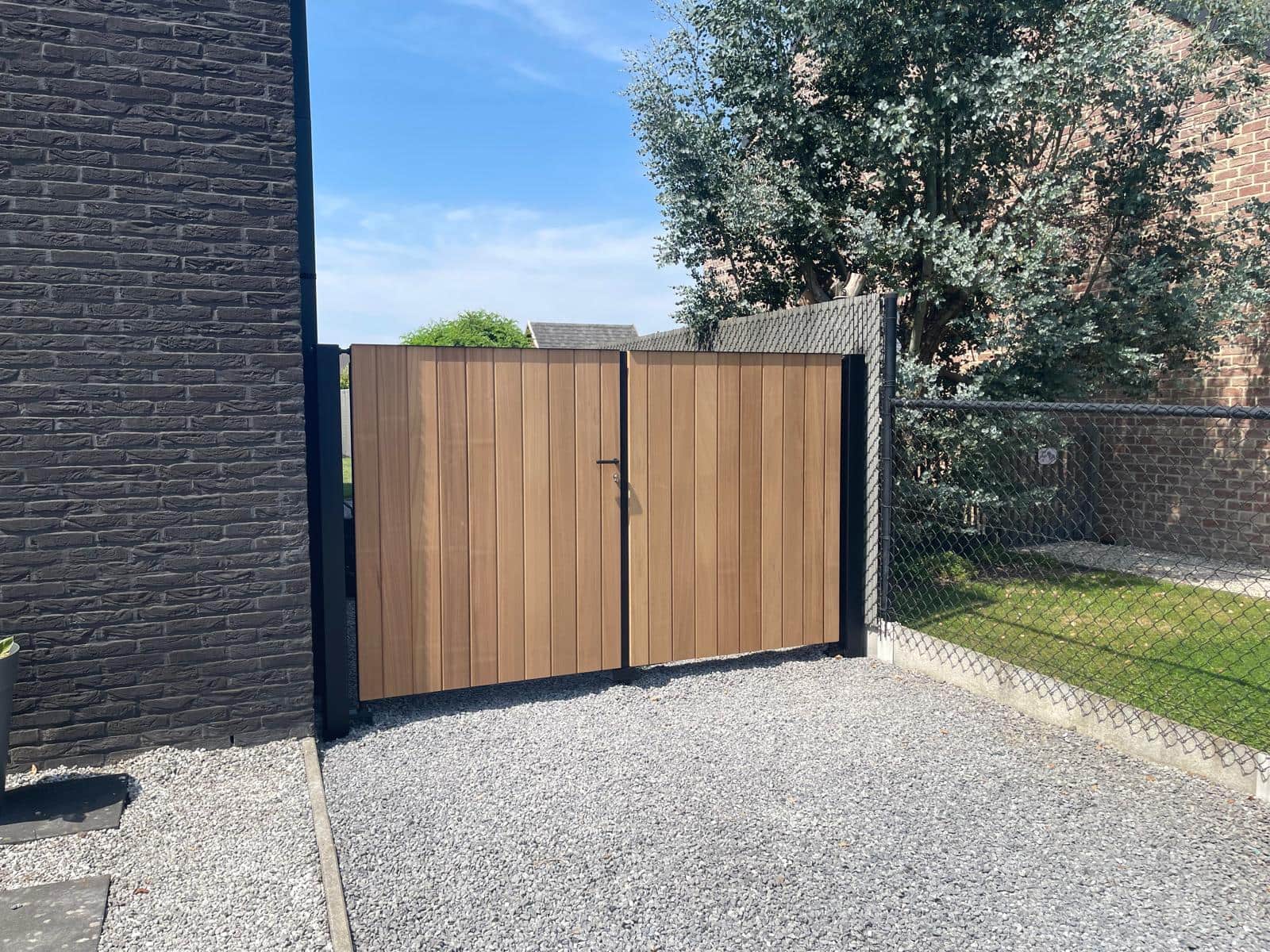 Hoekaanzicht van de gesloten houten poort met verticale Ayous-bekleding naast de tuin
