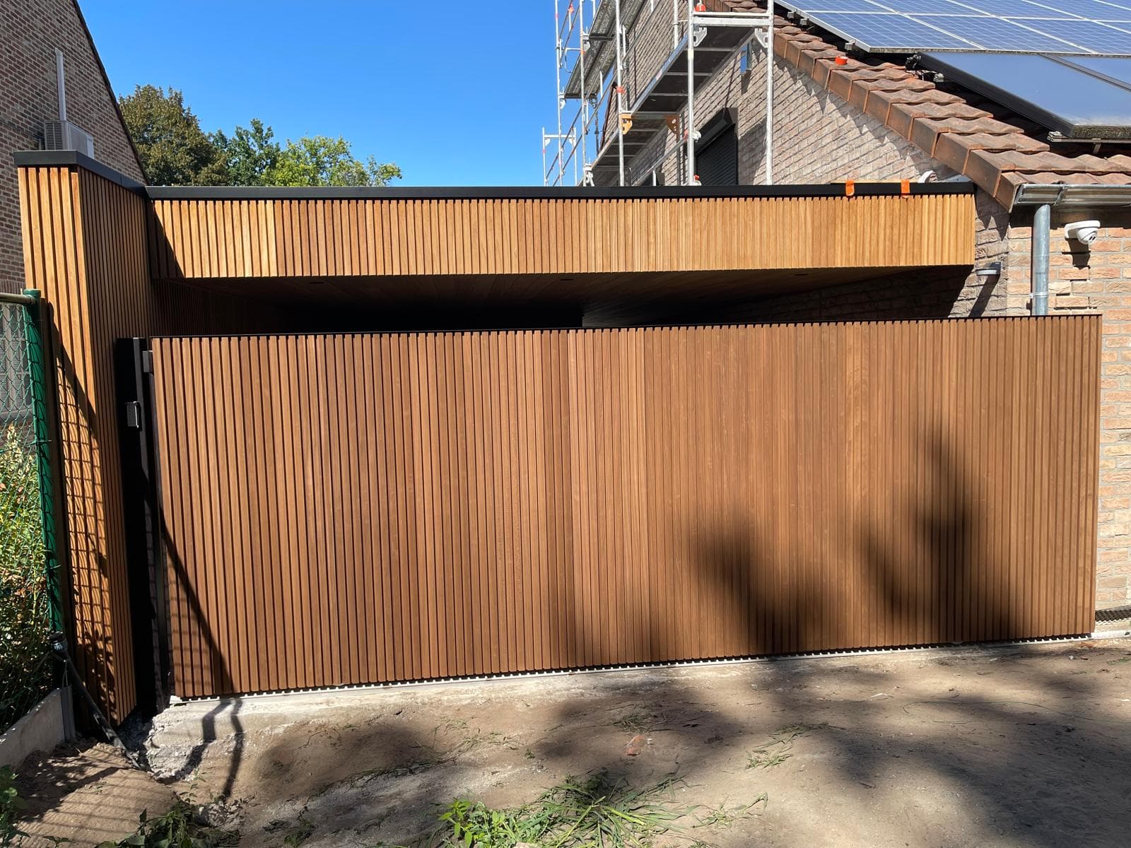 Frontaal aanzicht van de gesloten houten schuifpoort met carport