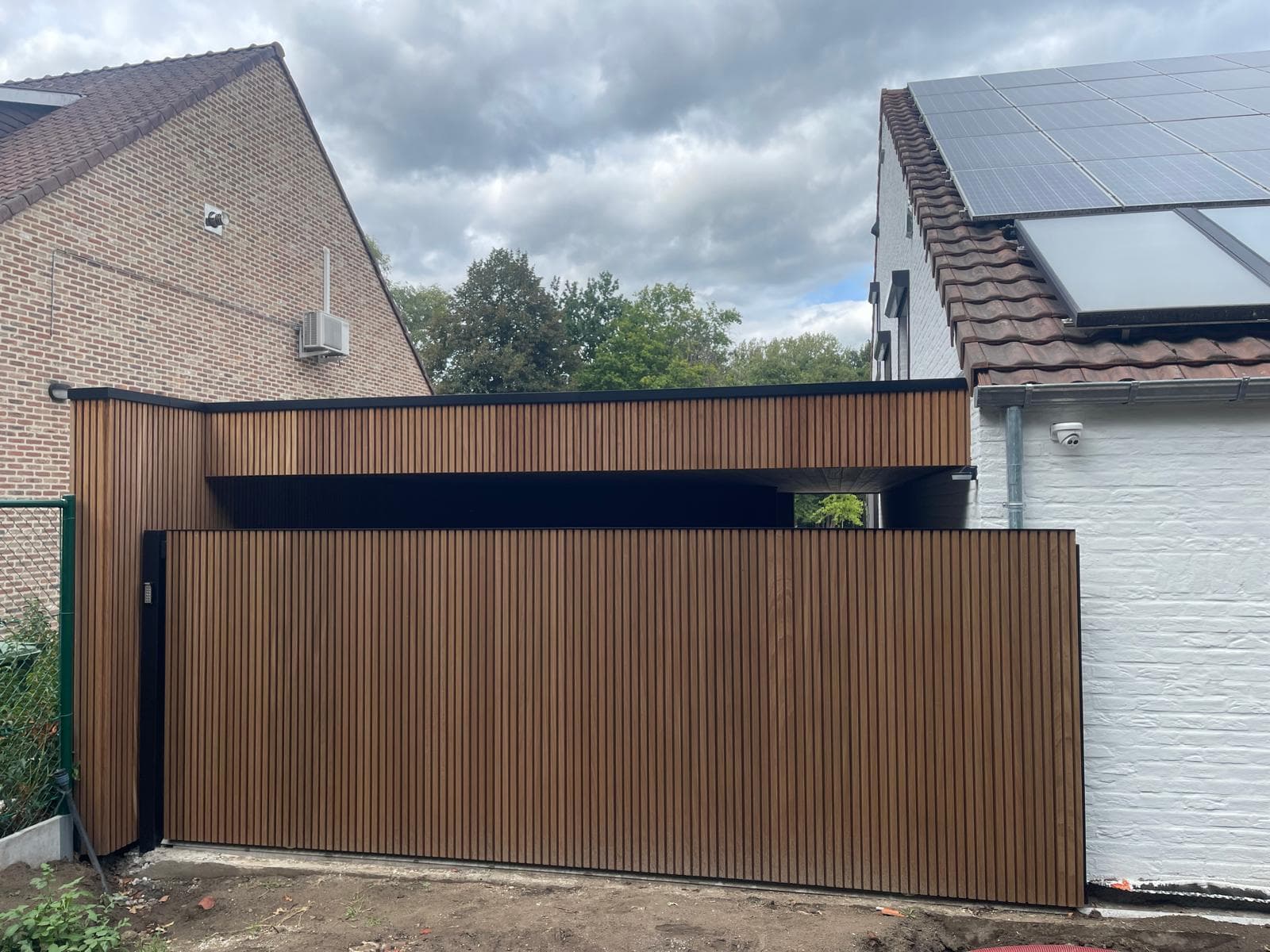 Zijaanzicht van de carport met houten gevelbekleding tussen twee woningen