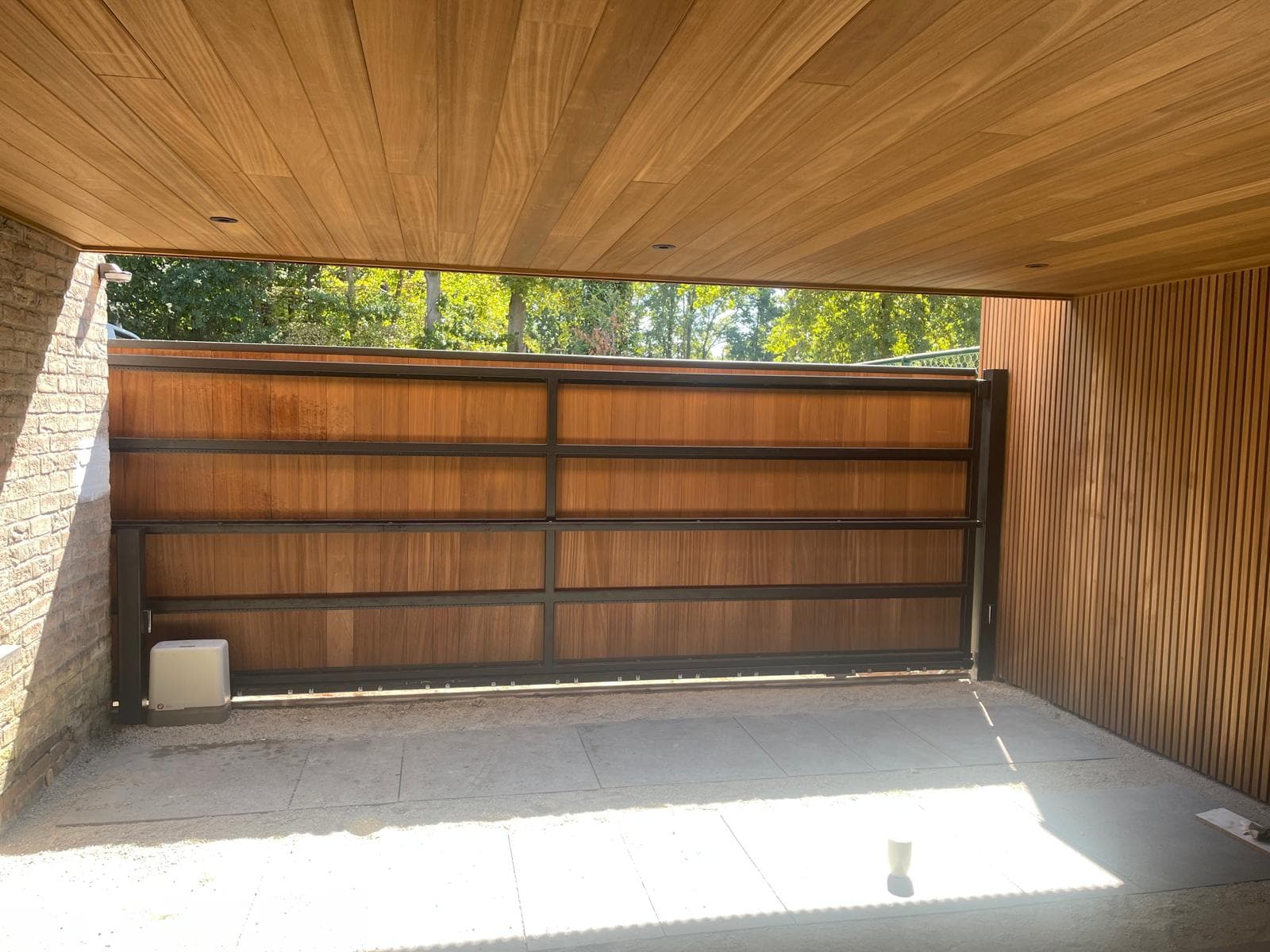 Binnenzicht van de carport met houten plafond en schuifpoort met zwart metaal