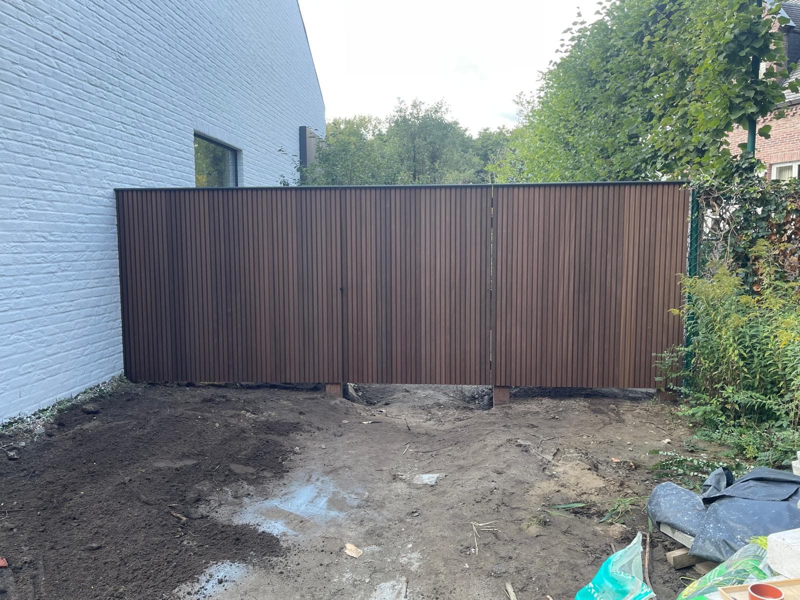 Volledige houten schutting met poortje langs een witte gevel