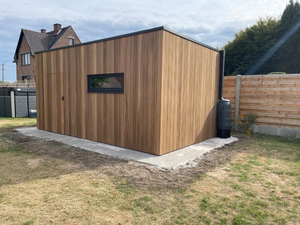 Voorgevel van de tuinberging met verborgen deur, zwart raam en regenton