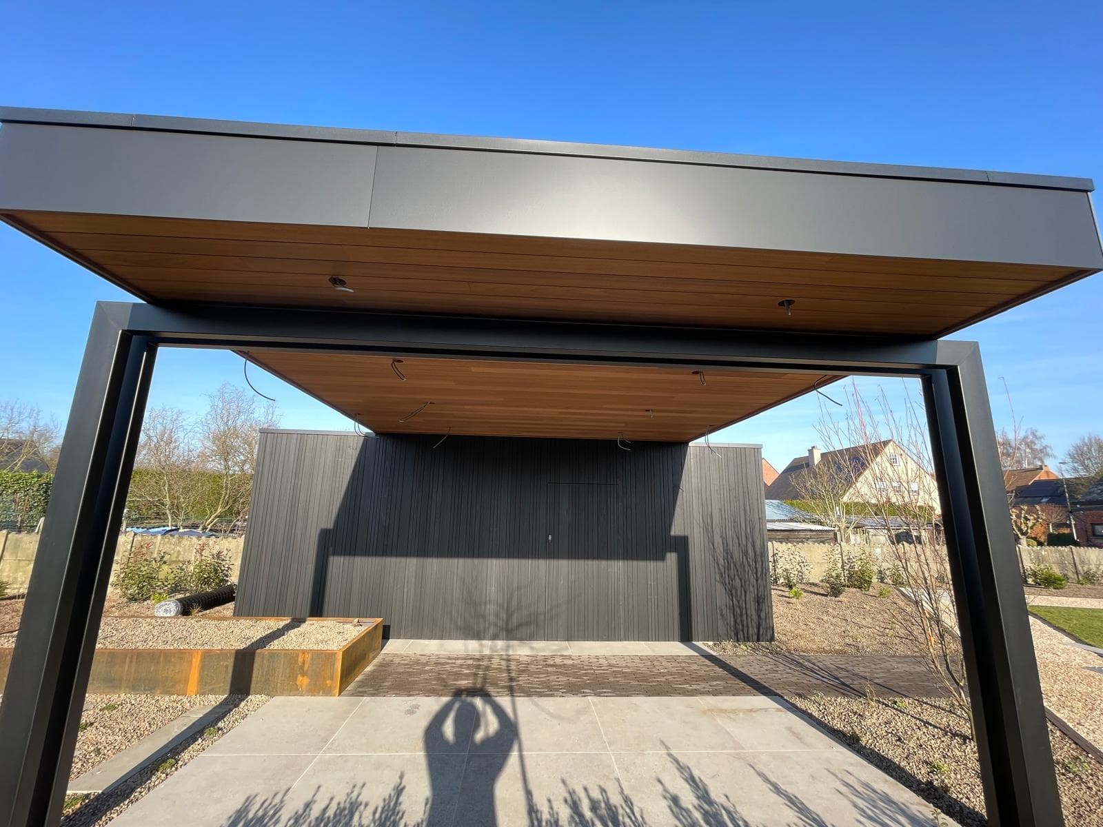 Symmetrisch zicht op de overkapping met houten plafond en zwart geoliede Ayous achterwand