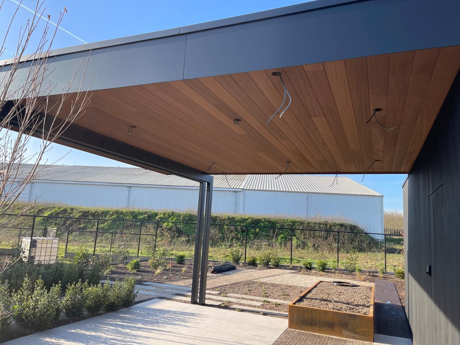 Hoek van de overkapping met houten plafond, cortenstalen plantbak en tuinpad