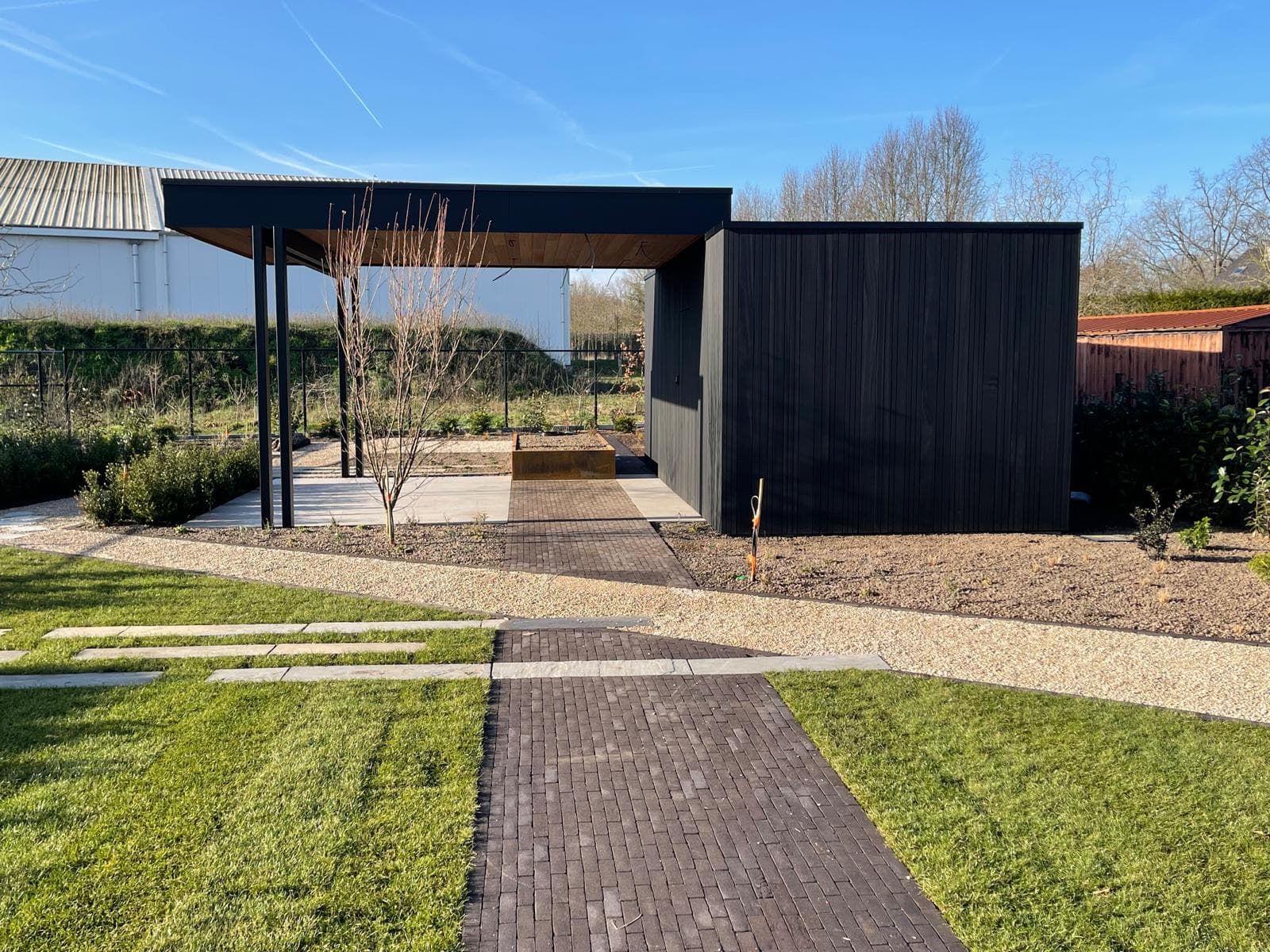 Totaalbeeld van de zwarte tuinberging met overkapping aan het einde van een siertuinpad