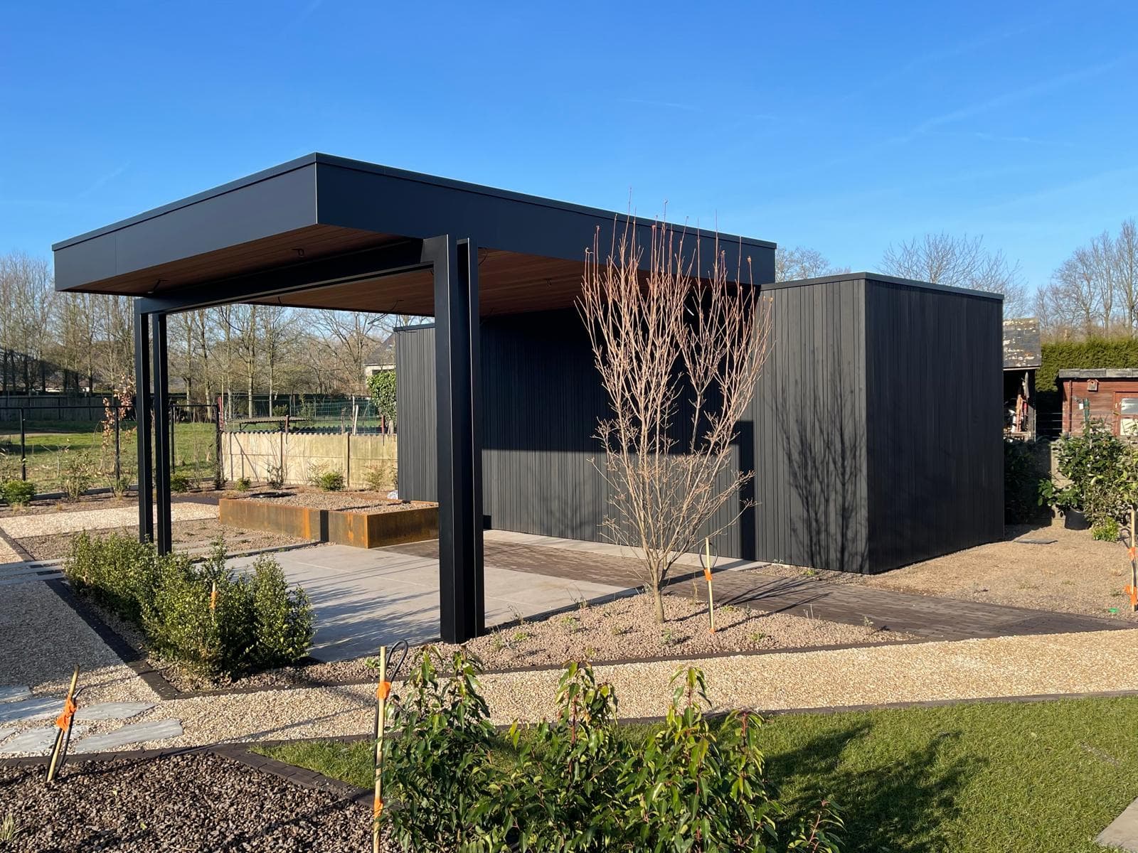 Moderne zwarte tuinberging met aangebouwde overkapping in een strakke tuin, WoPa Construction