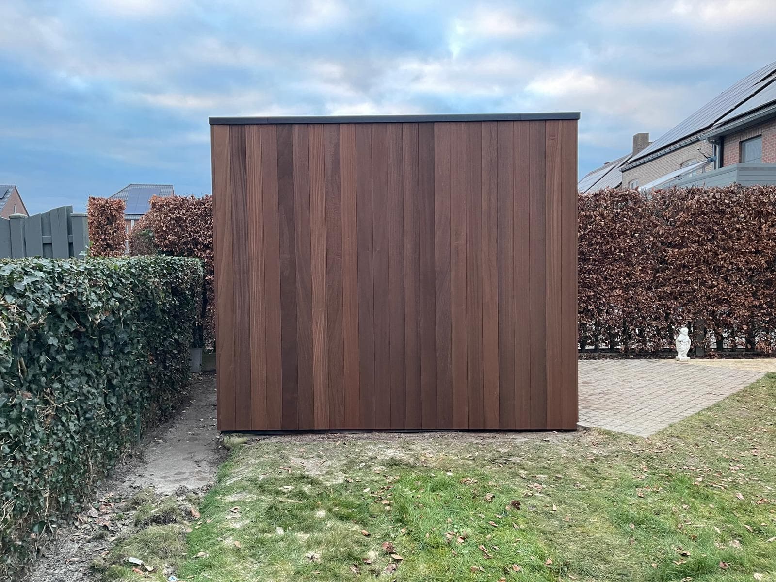 Zijaanzicht van het tuinhuisje met gesloten Ayous-houten gevel tussen hagen